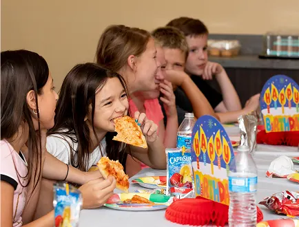 Children sitting at a café table eating pizza together at Dinotopia