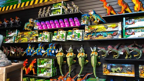 Souvenir shop shelves stacked with dinosaur figures, plush hatchlings and boxed dino toys